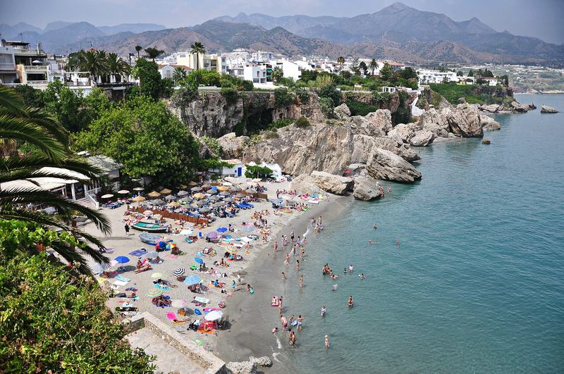 Der Strand Calahonda in Nerja mit Sonnenschirmen und weißen Häusern auf der Klippe
