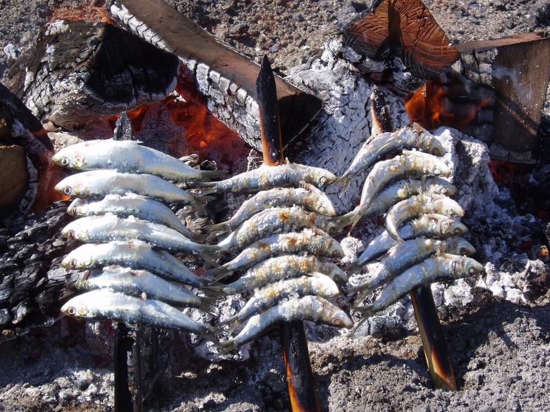 Sardinen-Espetos, im Sand aufgespießt, über der Holzglut am Strand gegrillt
