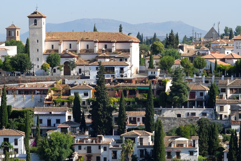 L’Albaicín vu de l’Alhambra : maisons blanches, cyprès et l’église San Nicolás au sommet, avec la sierra au fond