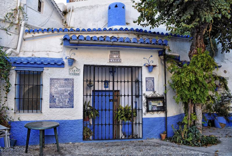 La façade blanchie à la chaux d’une maison-grotte du Sacromonte, avec porte et grilles bleues et des plantes à l’entrée